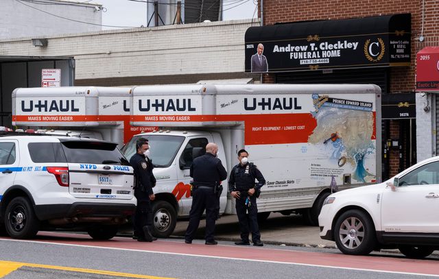 Police officers in masks stand in front of two U-Haul trucks parked on the sidewalk